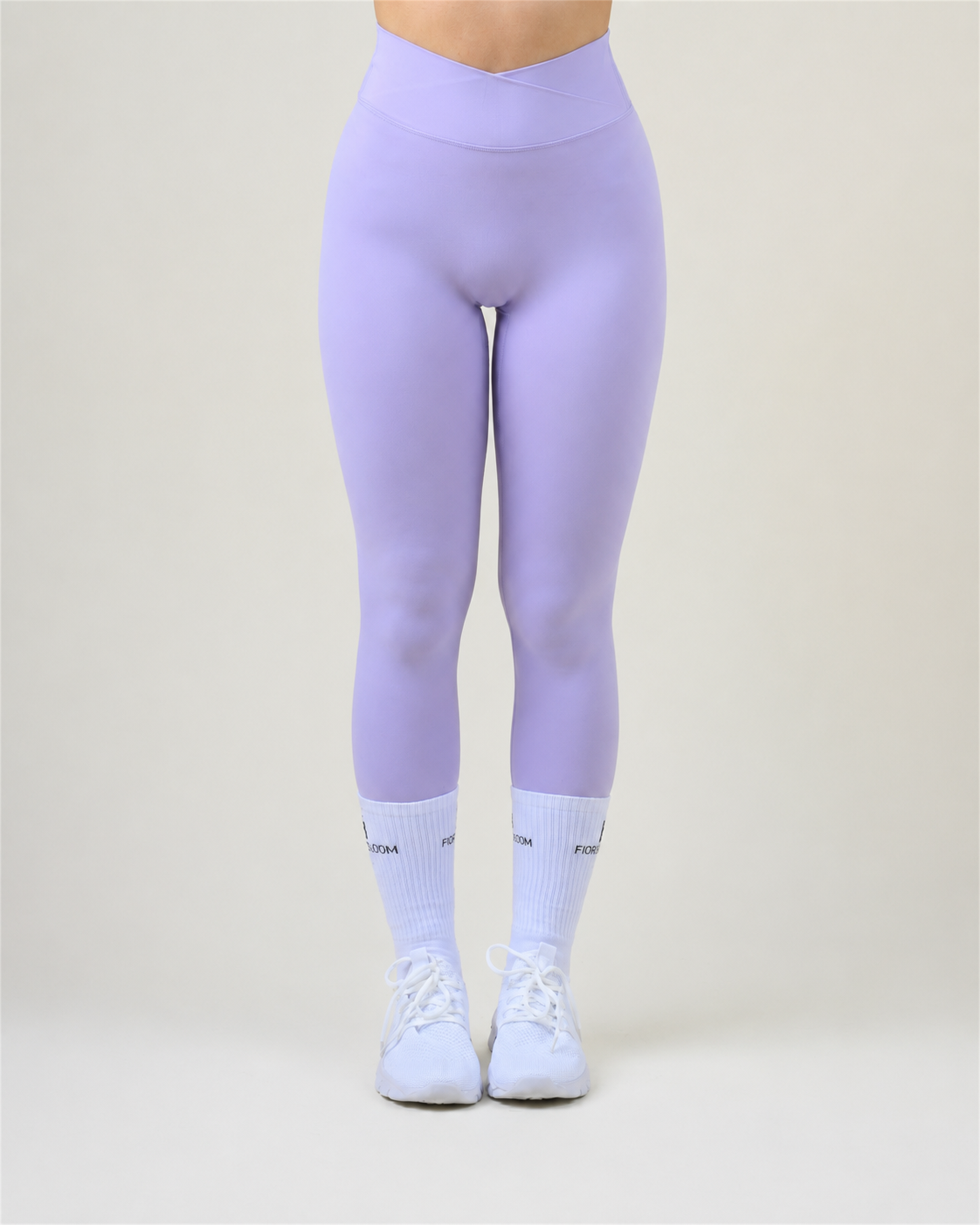 SoftForm V-Shape Leggings in Lila von Fiora Bloom – Titelbild, Frontansicht der Beine vor hellem Studiohintergrund, V-förmiger Bund sichtbar, dazu weisse Fiora Bloom Socken und weisse Sneaker.