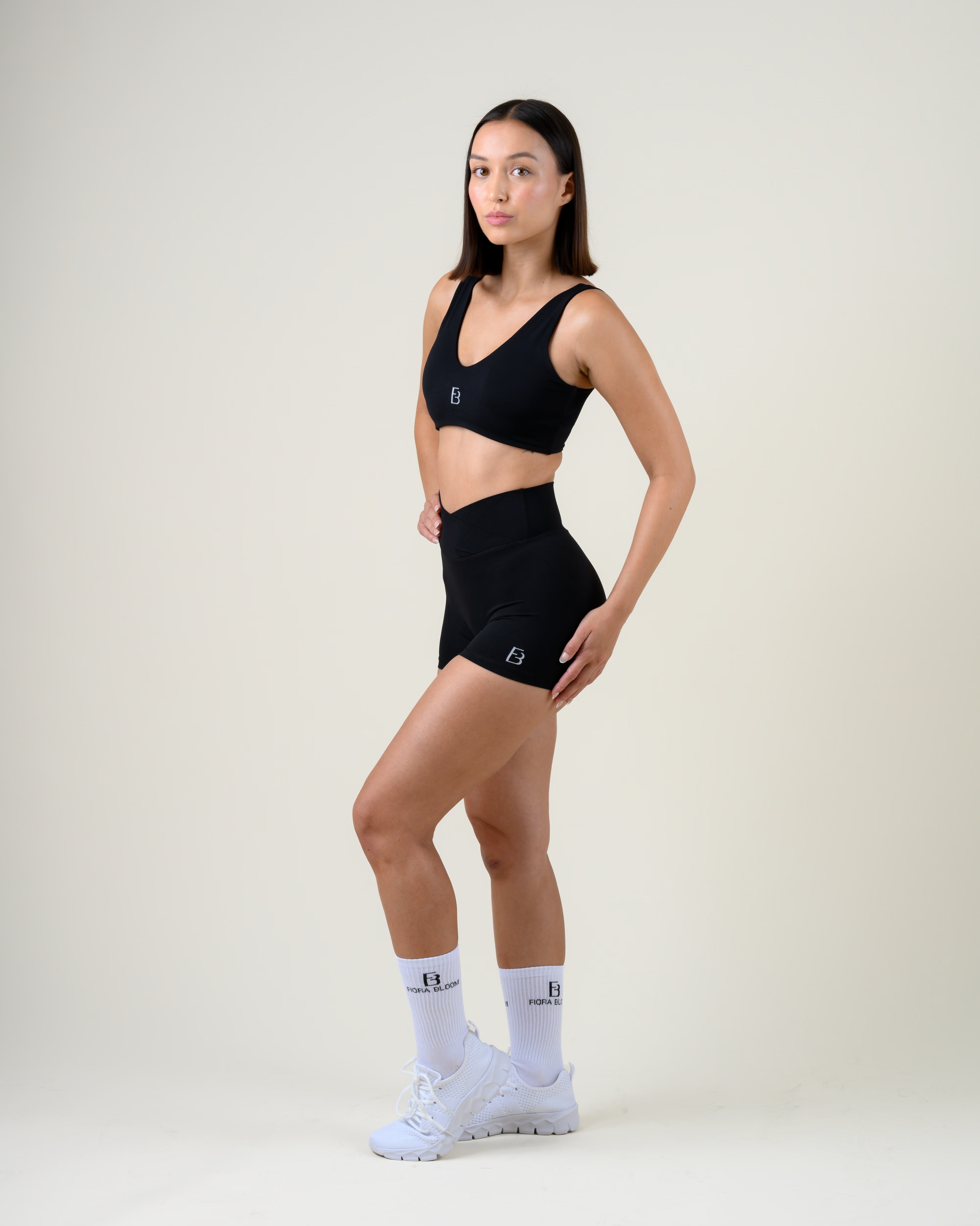 Soft Form V-Shape Shorts in Schwarz von Fiora Bloom – Ganzkörper-Look in Dreiviertelansicht, kombiniert mit dem Soft Form V-Top in Schwarz, weisse Socken und Sneaker.
