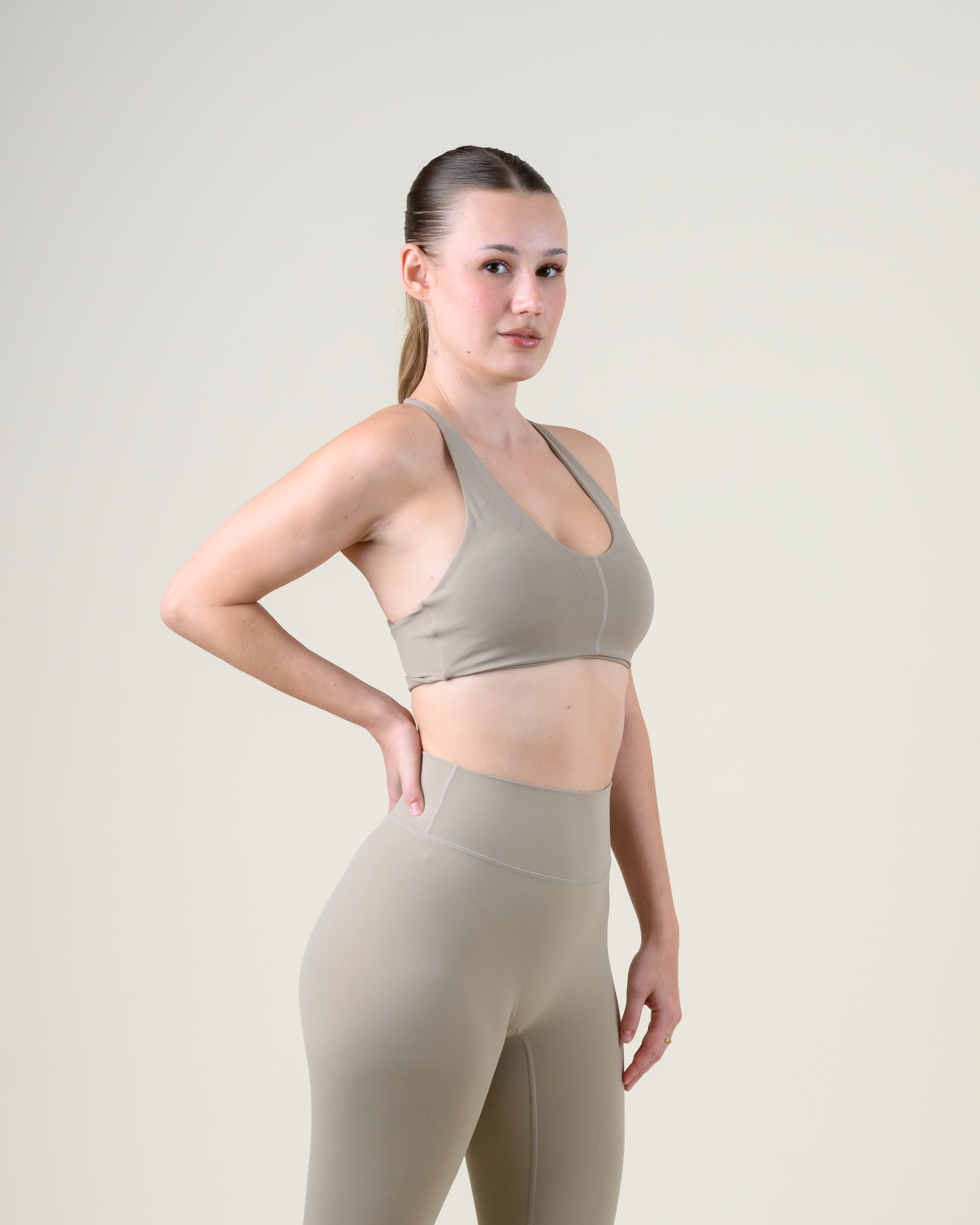 Soft Form Basic Top in Taupe von Fiora Bloom – Dreiviertelansicht von vorne, zweite Pose, Hand in der Taille, Passform an Brust und Taille sichtbar.