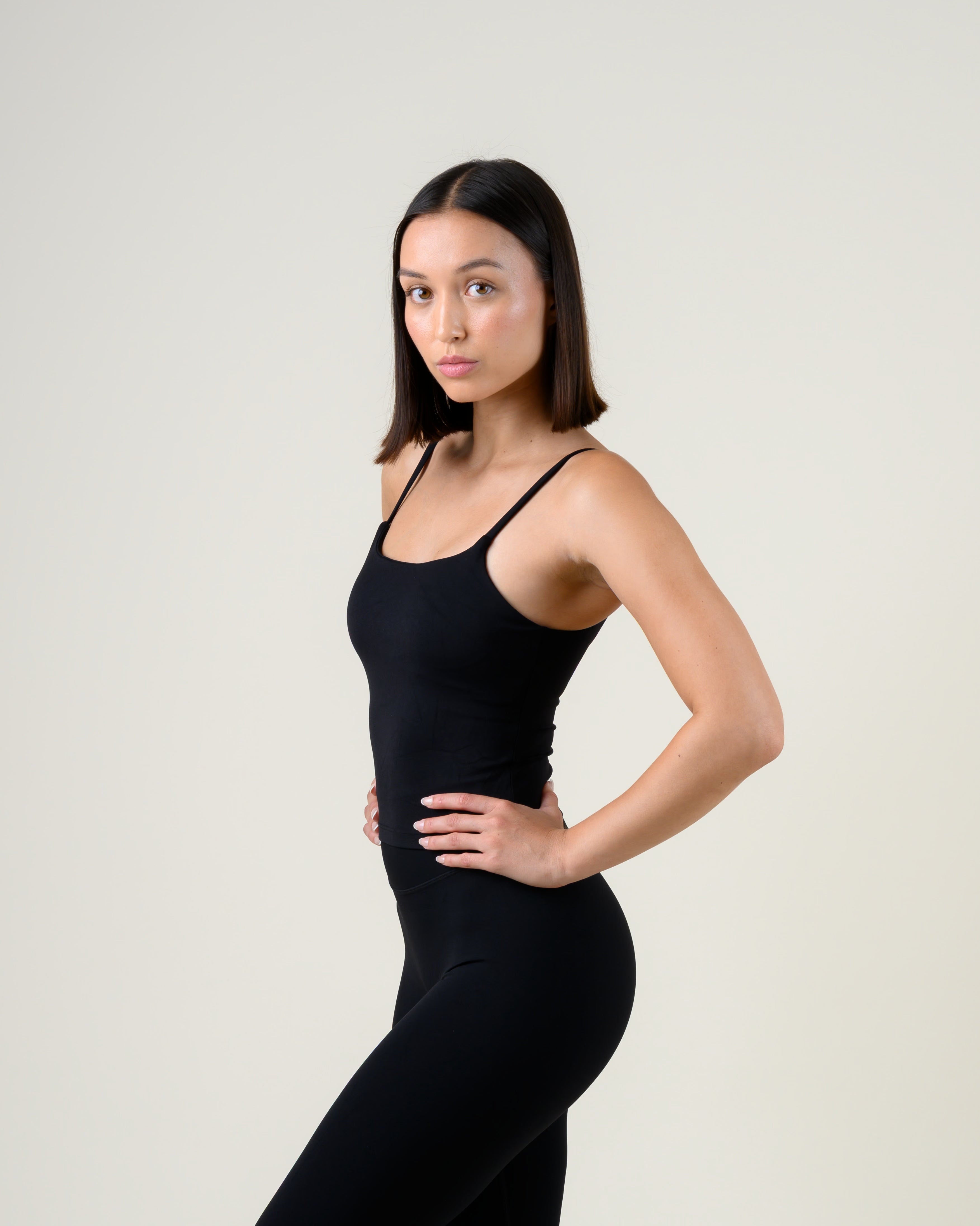 Soft Form Tanktop in Schwarz von Fiora Bloom – Dreiviertelansicht von vorne, Hand in der Taille, Sitz an Brust und Taille sichtbar.
