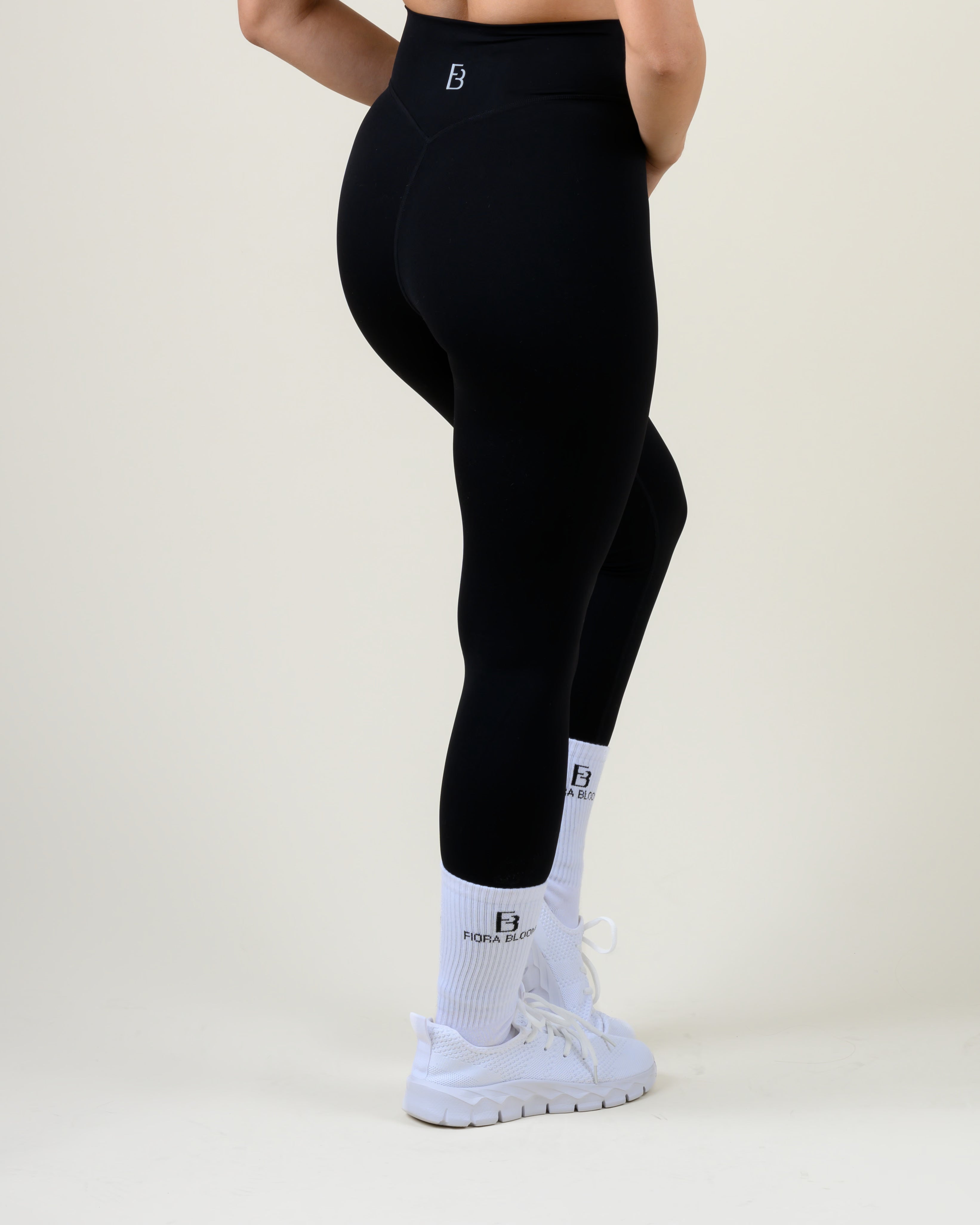 Soft Form V-Shape Leggings in Schwarz von Fiora Bloom – Dreiviertelansicht von hinten in Bewegung, Bein angewinkelt, Sitz an Gesäss und Oberschenkel sichtbar.