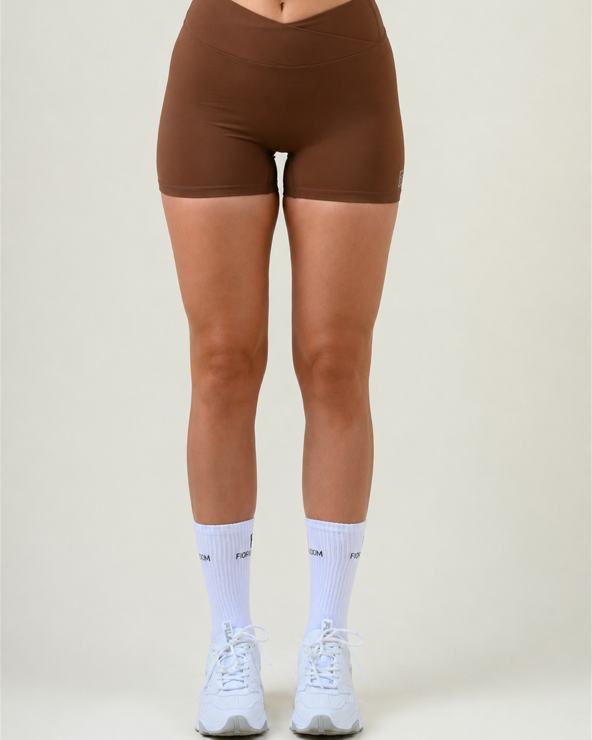 SoftForm V-Shape Shorts in Espresso von Fiora Bloom – Titelbild, Frontansicht vor hellem Studiohintergrund, V-förmiger Bund und kurze Beinlänge sichtbar, kombiniert mit einem passenden Oberteil in Espresso, weissen Fiora Bloom Socken und weissen Sneakern.